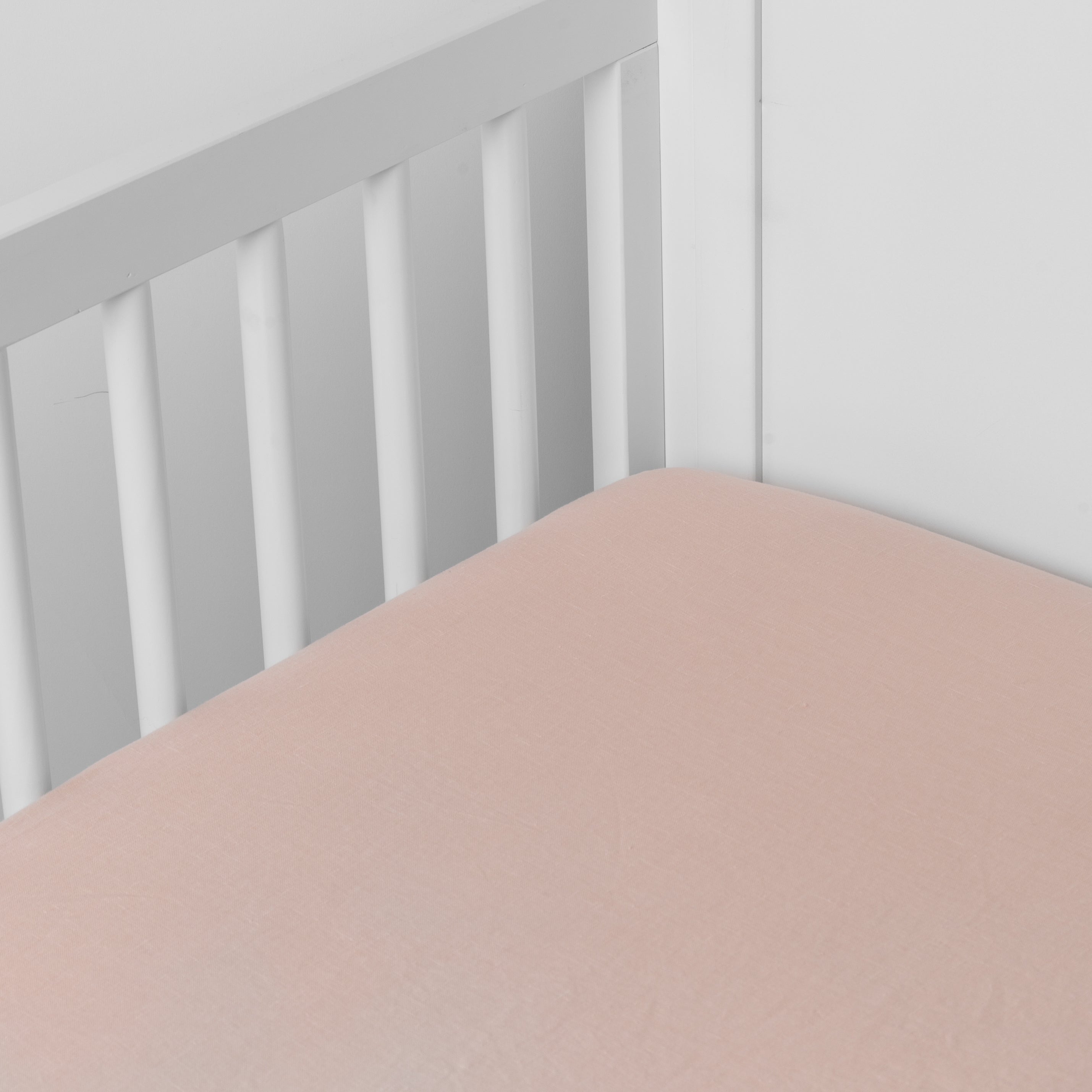 Pearl: linen crib sheet on the mattress shot slightly overhead into the corner of a white crib. against a white background.