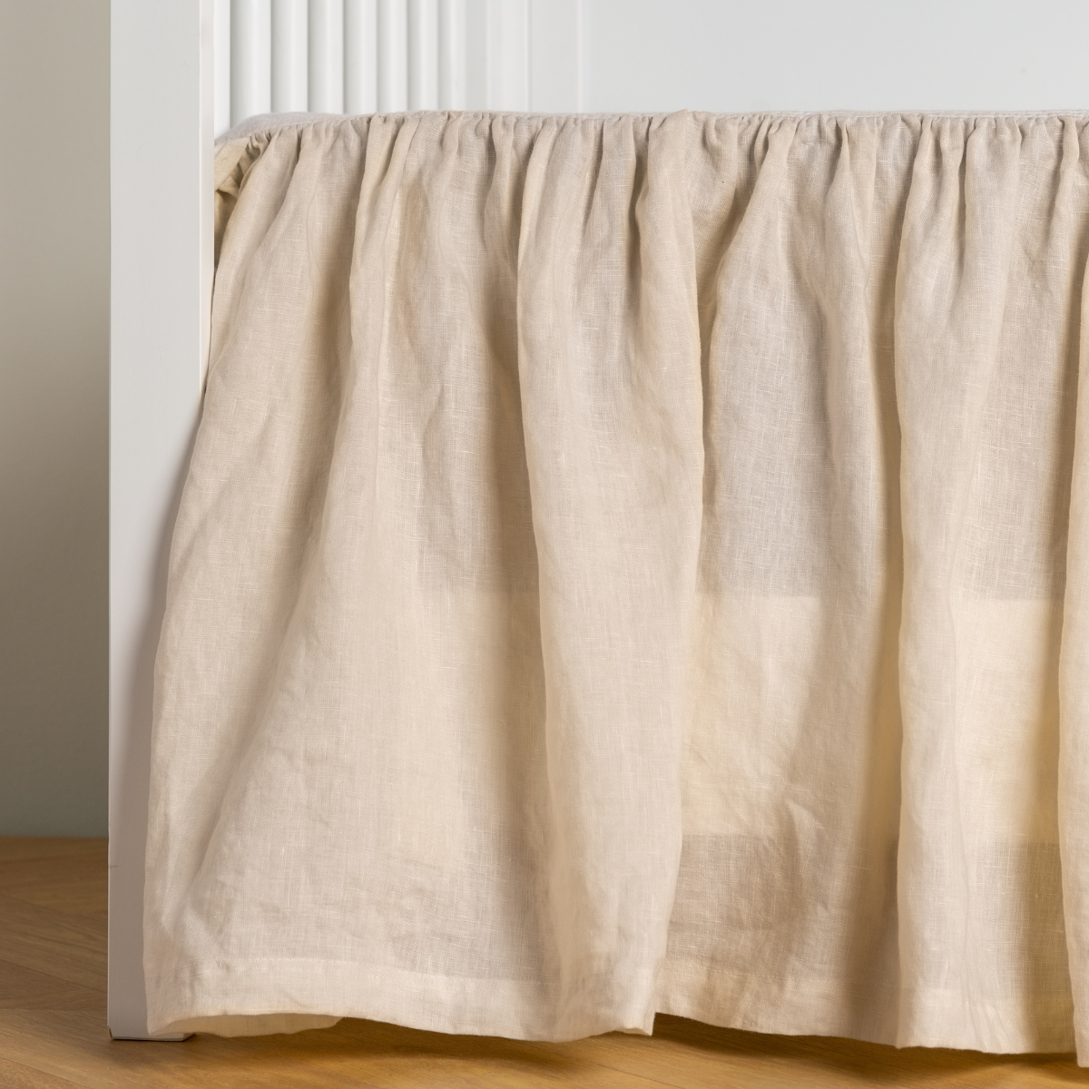 Parchment: crib skirt shown on a white crib with no mattress against a white wall and medium wood flooring.