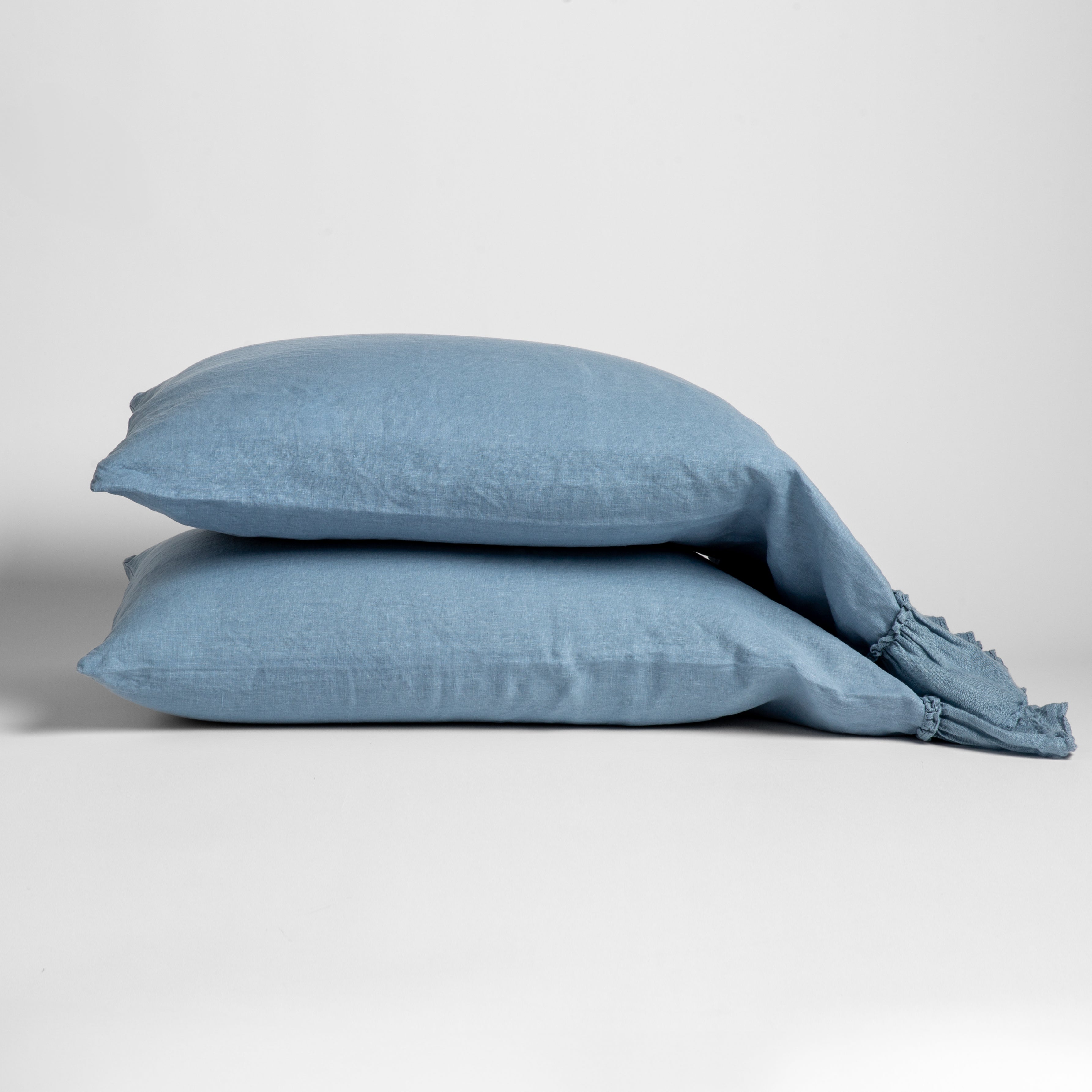 Tahoe Blue: Two sleeping pillows stacked at a slight angle against a plain background, showcasing ruffle trim detail - side view.