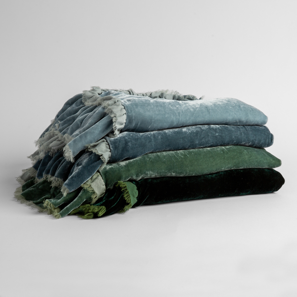 : a stack of four silk velvet blankets in cloud, mineral, eucalyptus and jade.