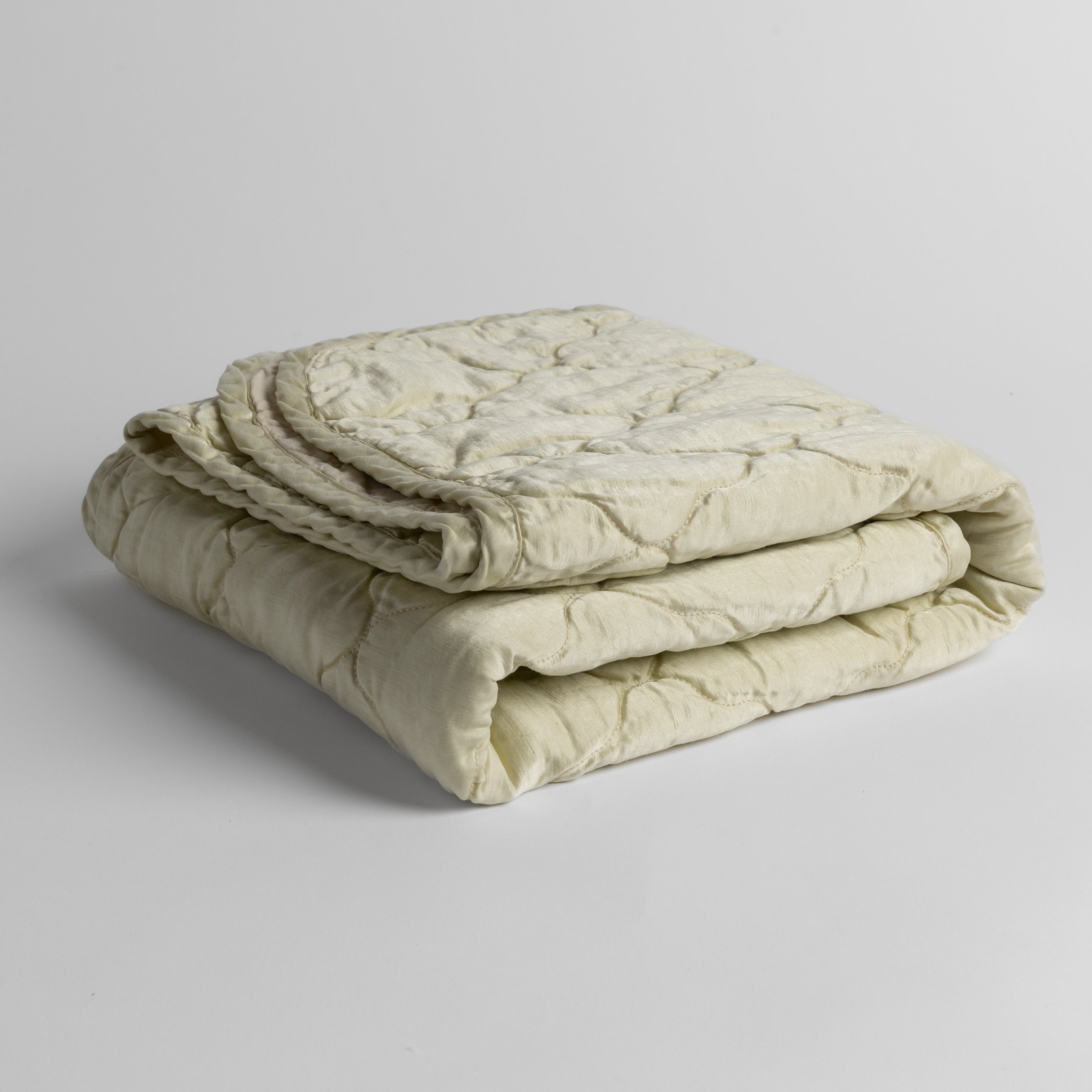 Parchment: quilted charmeuse blanket folded and shown against a white background from a slight overhead angle.
