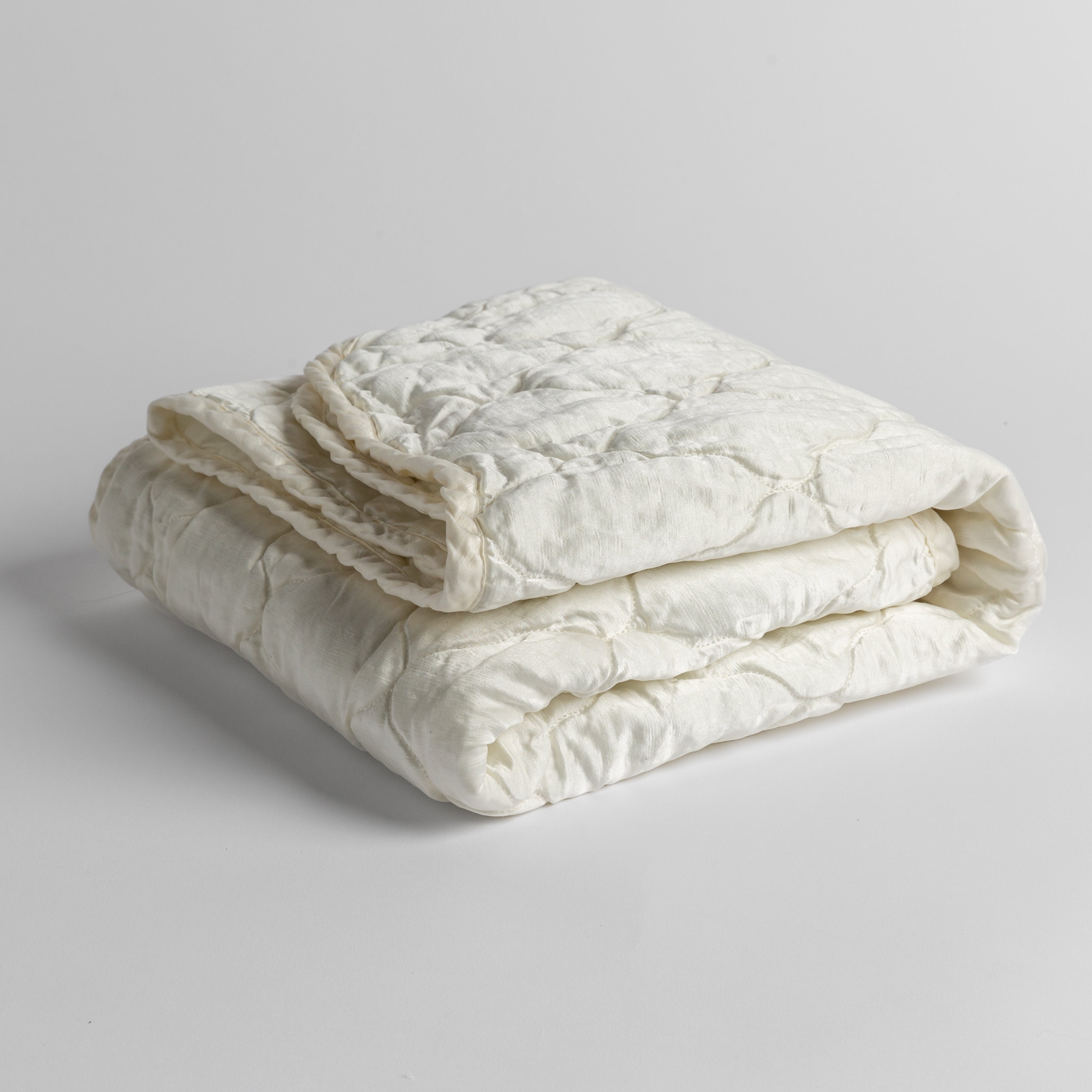 Winter White: quilted charmeuse blanket folded and shown against a white background from a slight overhead angle.