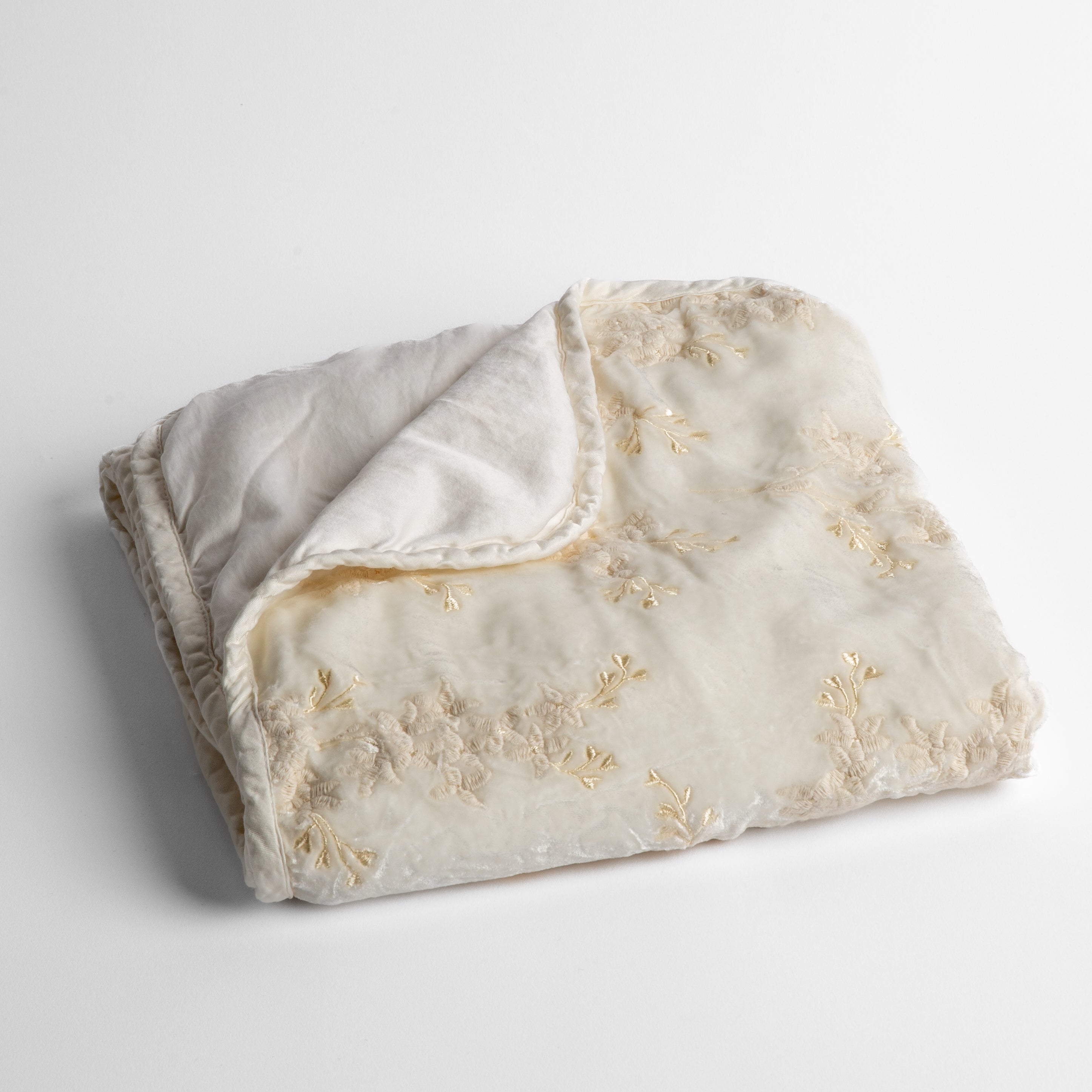 Winter White: embroidered silk velvet baby blanket folded with a corner folded back to show the trim and back of the blanket - shot overhead at a slight angle against a white background.