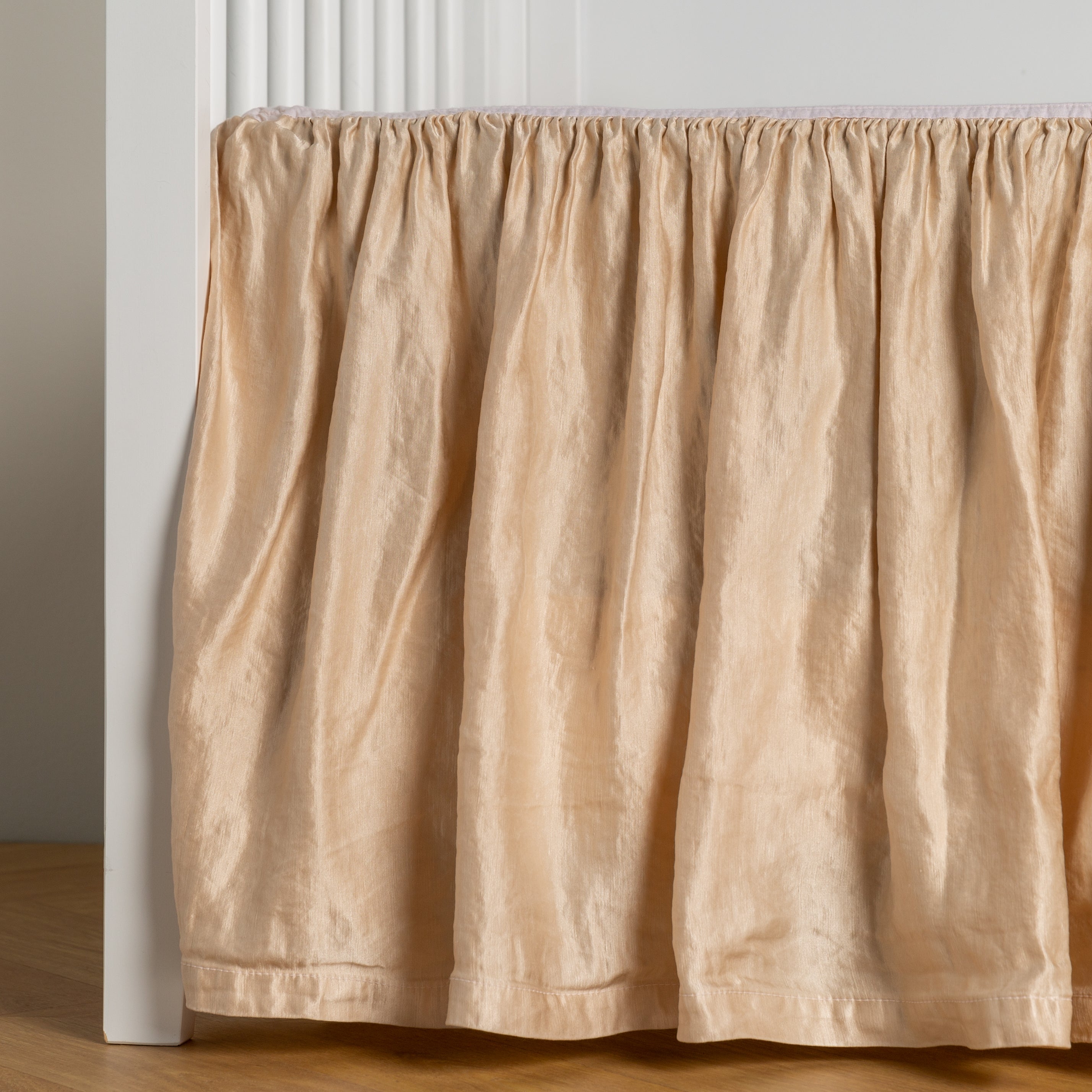 Pearl: charmeuse crib skirt shown on a white crib against a white wall and medium wood floor.