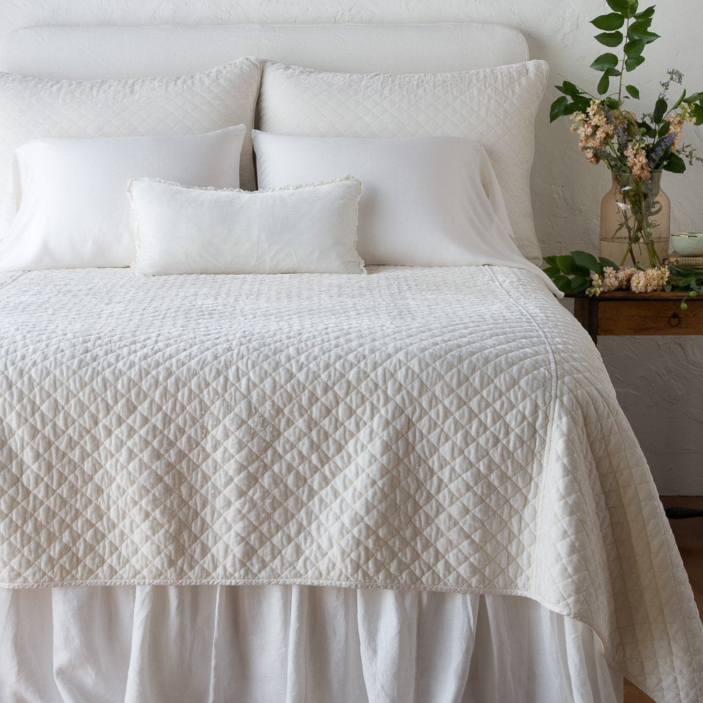 : Silk velvet quilted coverlet on a neatly made, winter white bed - end of bed view.