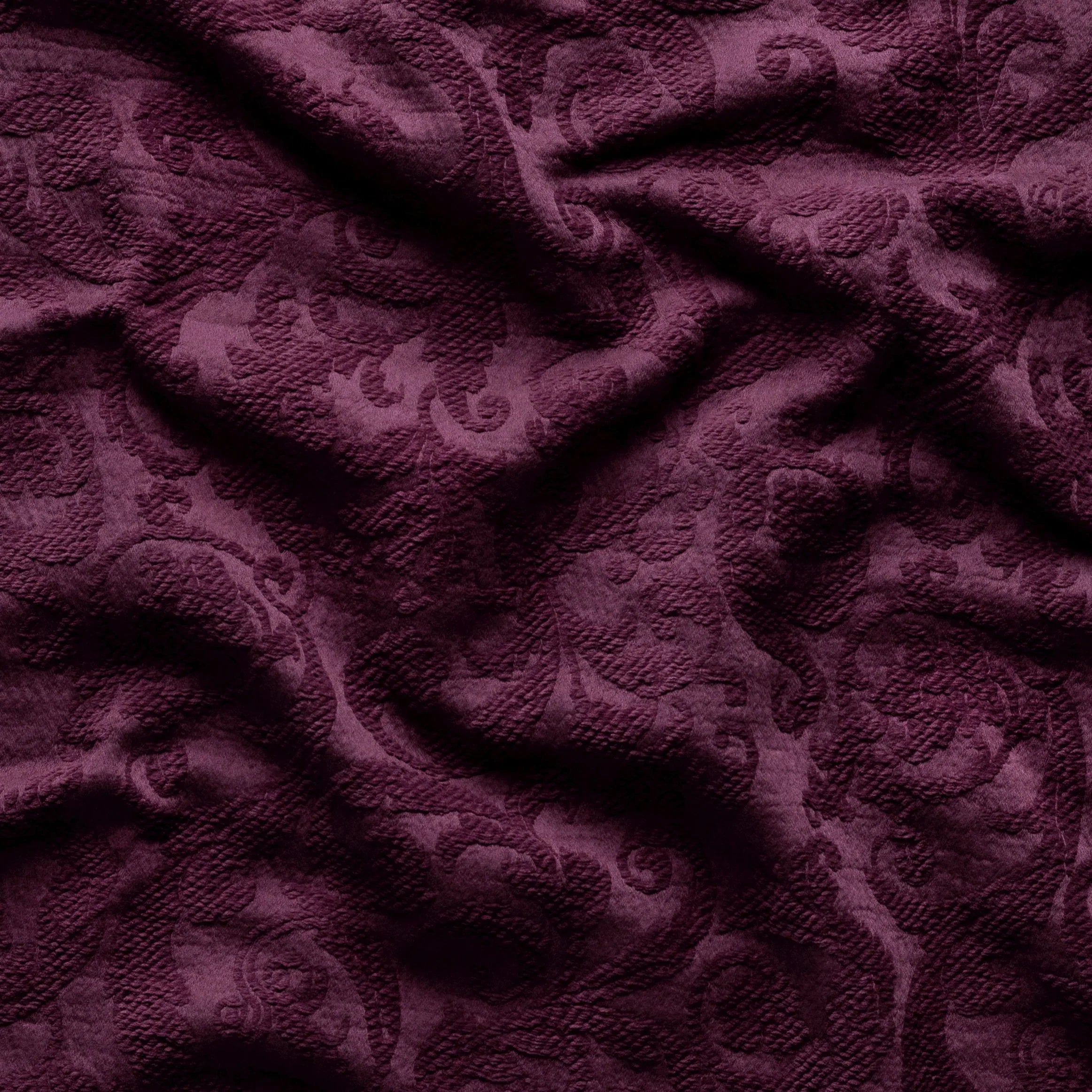 Fig: A close up of Adele fabric in fig, a richly saturated purple-garnet. The fabric is rumpled to show the cotton damask texture.