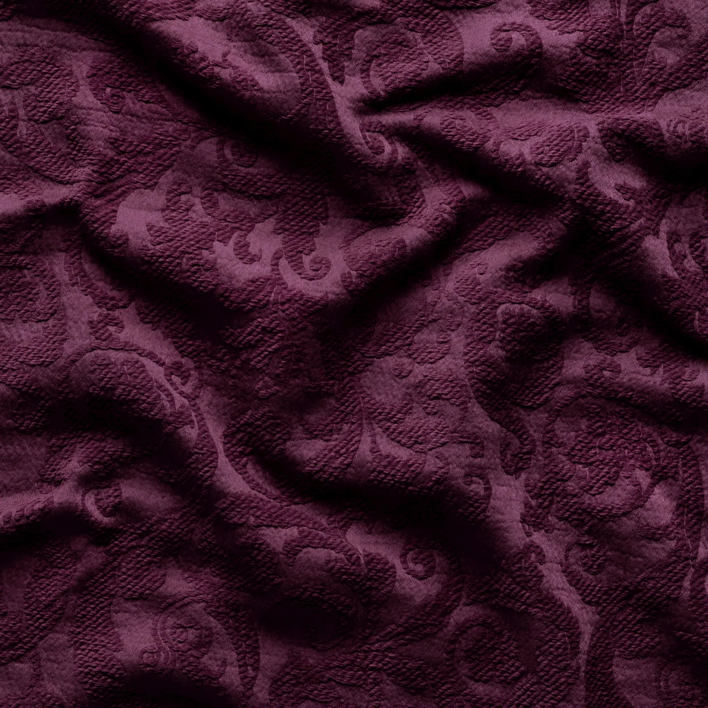 Fig: A close up of Adele fabric in fig, a richly saturated purple-garnet. The fabric is rumpled to show the cotton damask texture.