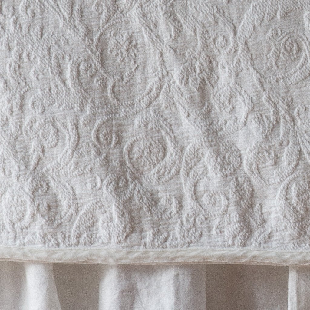 Winter White: Close up of the Adele coverlet in winter white, highlighting the detail of the cotton damask and the silk velvet edging trim. A winter white bed skirt peeks out at the bottom of the shot.