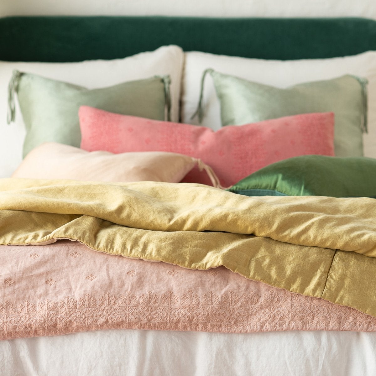 : Ines throw blanket in rouge, layered under green, pink, and gold tones on a white bed, - cropped end of bed view.