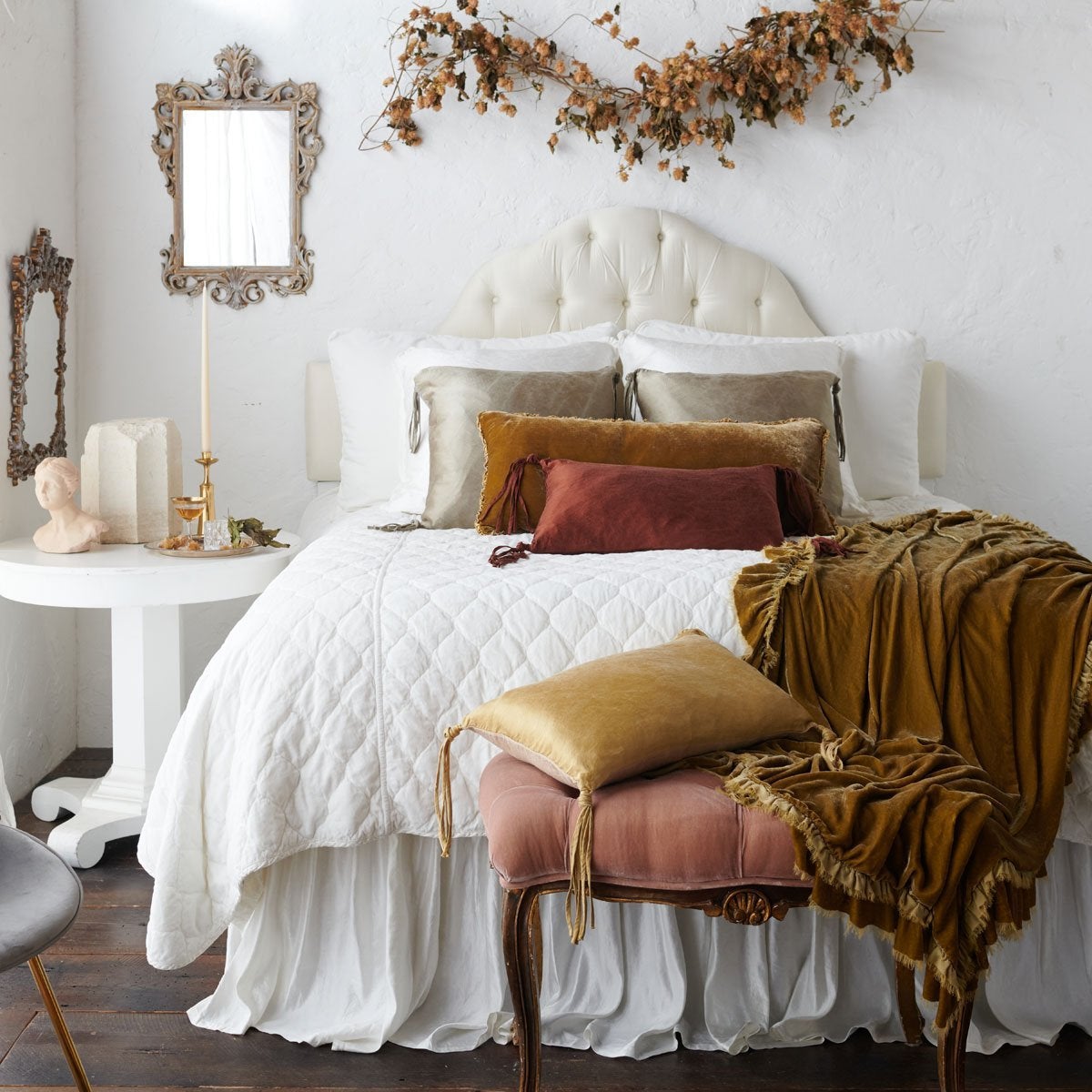 : Mixed textures of silk velvet, silk charmeuse, and quilted cotton velvet on a grand, elegant white bed with brown and gold accents. The honeycomb Loulah throw blanket is draped over the corner onto an antique pink velvet bench.