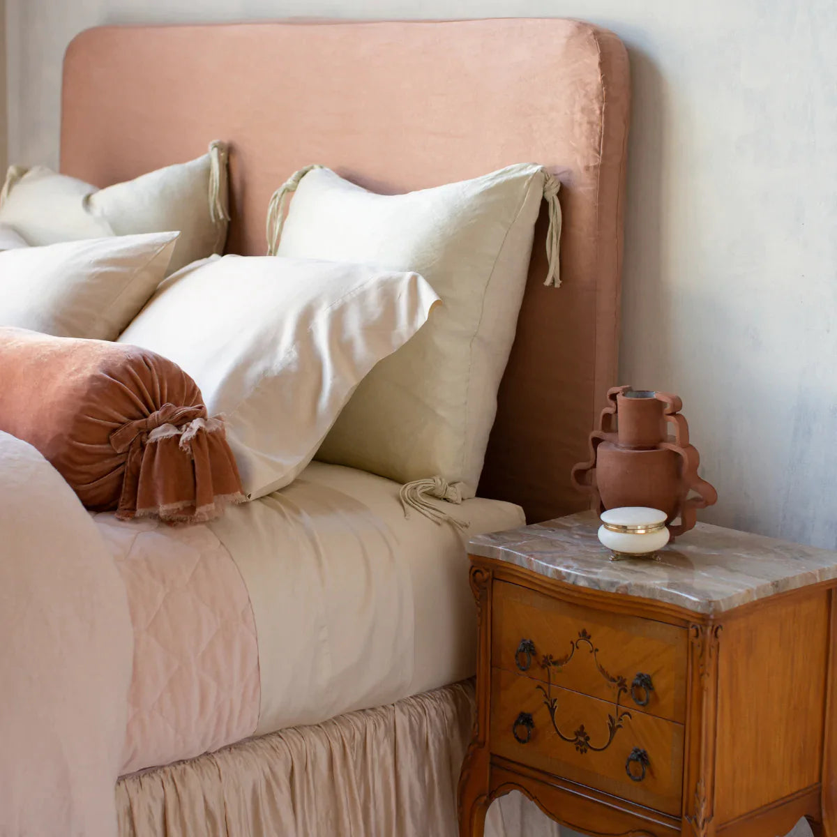 : Bria fitted sheet in parchment shown from a three quarter cropped angle. The cotton sateen sheets are layered with cotton velvet, silk velvet, and silk charmeuse in soft pink and cream tones.