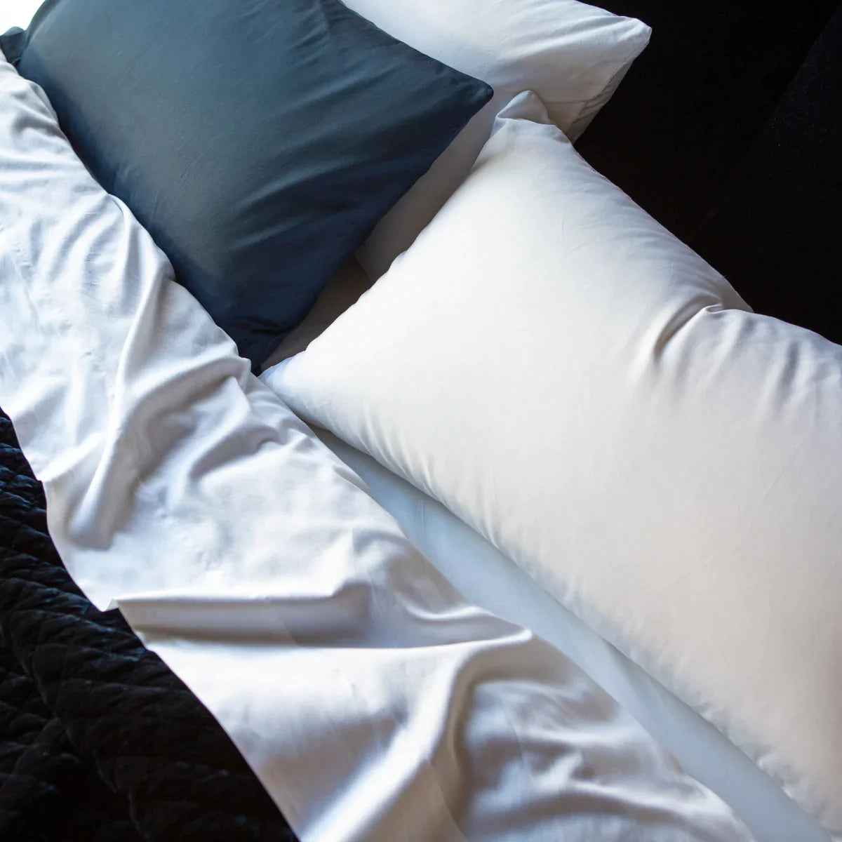 : Bria flat sheet in white, shown folded over a coverlet from an overhead angle, with side by side sleeping pillows in white and midnight blue.