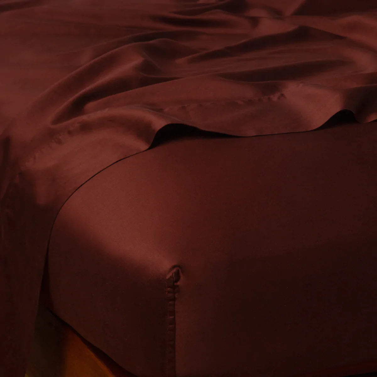 Mahogany: Cotton sateen flat sheet draped over matching fitted sheet. Shown from the top corner, the flat sheet is rumpled, highlighting the shine of the fabric.