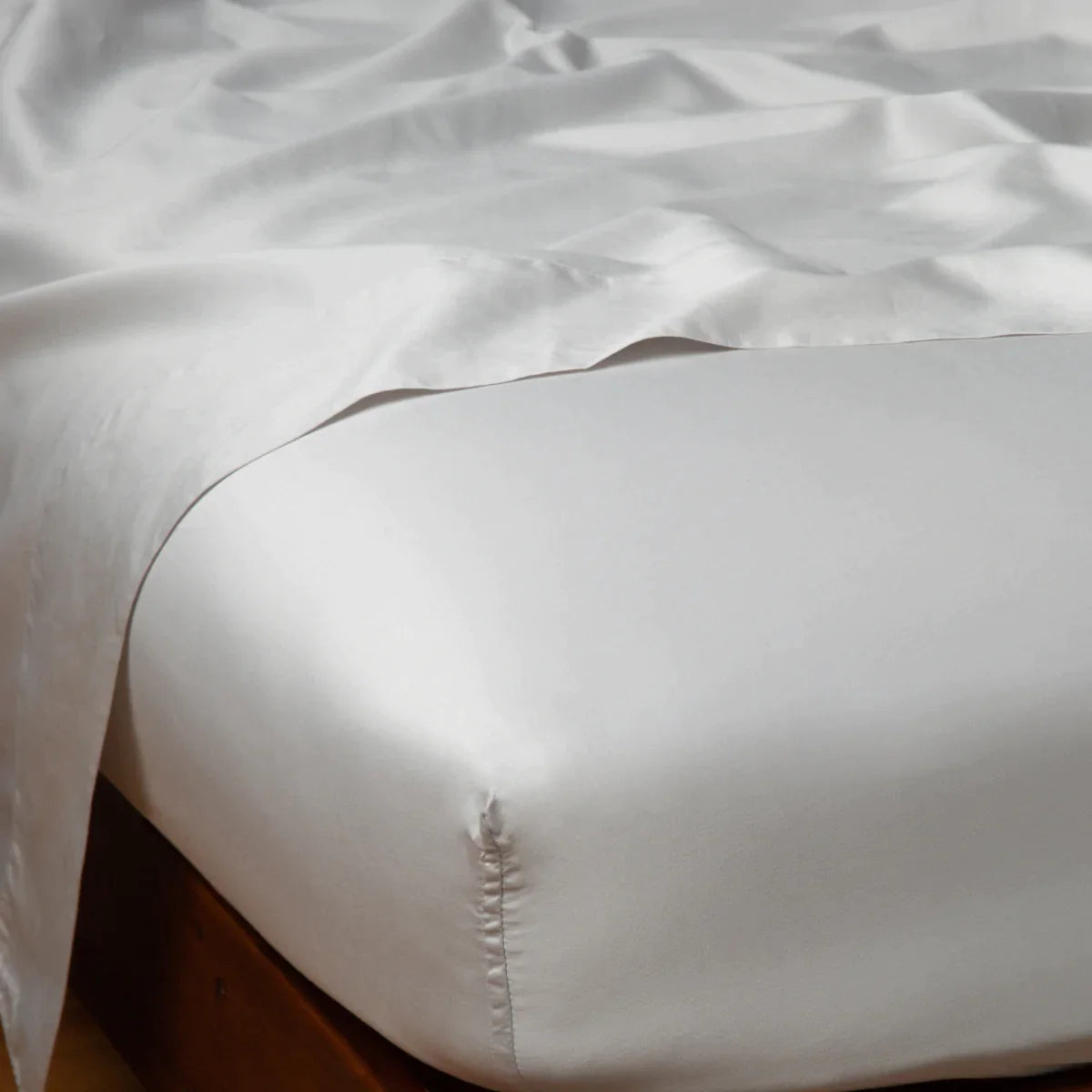 Sterling: Cotton sateen flat sheet draped over matching fitted sheet. Shown from the top corner, the flat sheet is rumpled, highlighting the shine of the fabric.