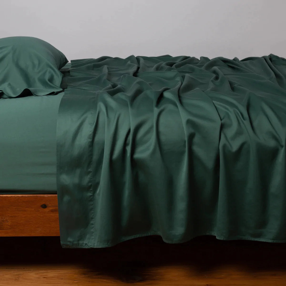 Jade: Cotton sateen sleeping pillow, on a bed with matching sheets - side view.