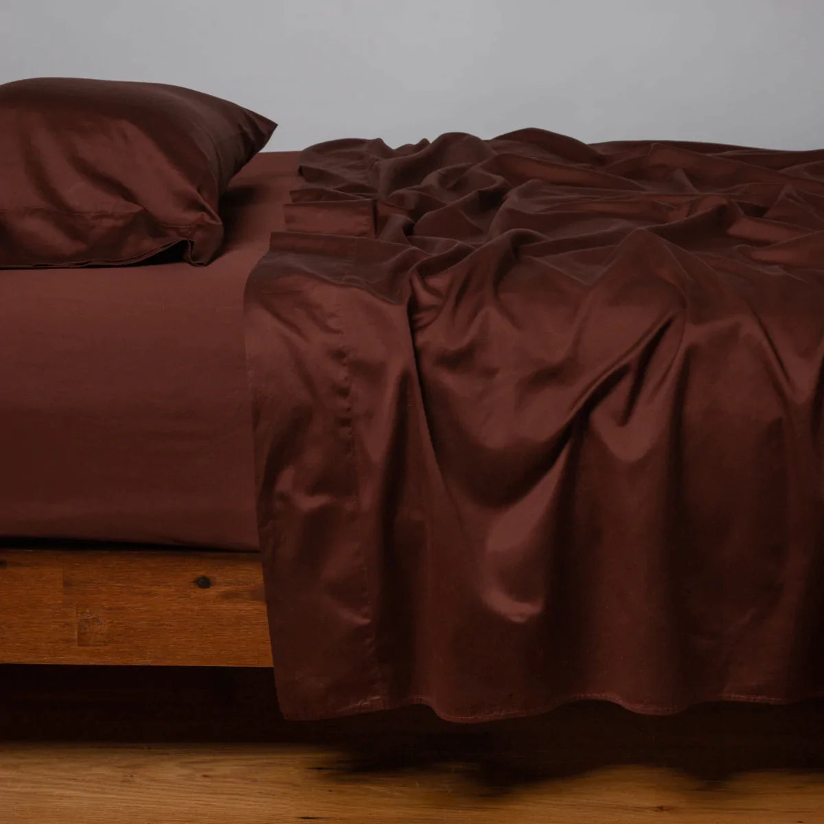 Mahogany: Cotton sateen sleeping pillow, on a bed with matching sheets - side view.