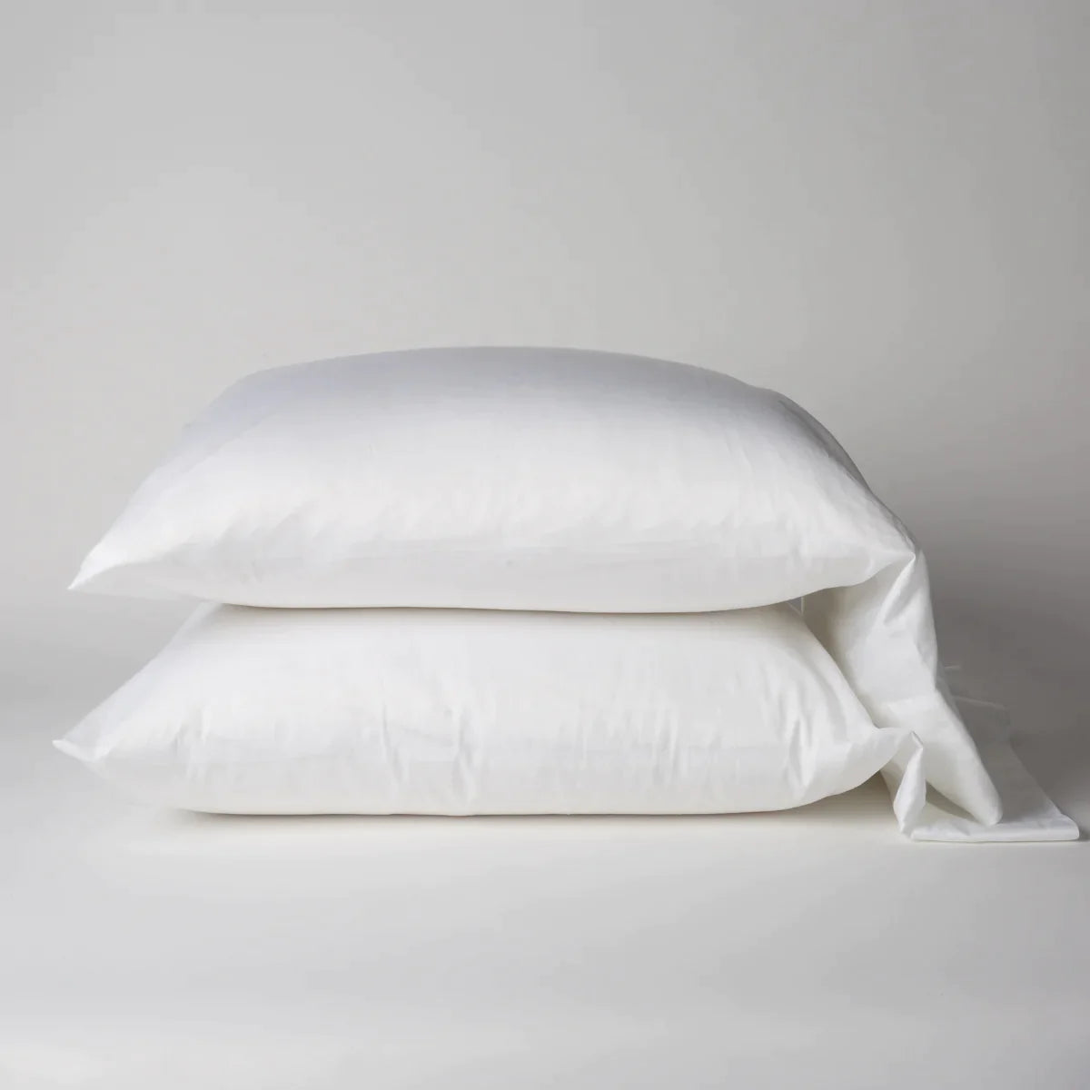 White: Two cotton sateen sleeping pillows, stacked neatly against a white backdrop - side view.