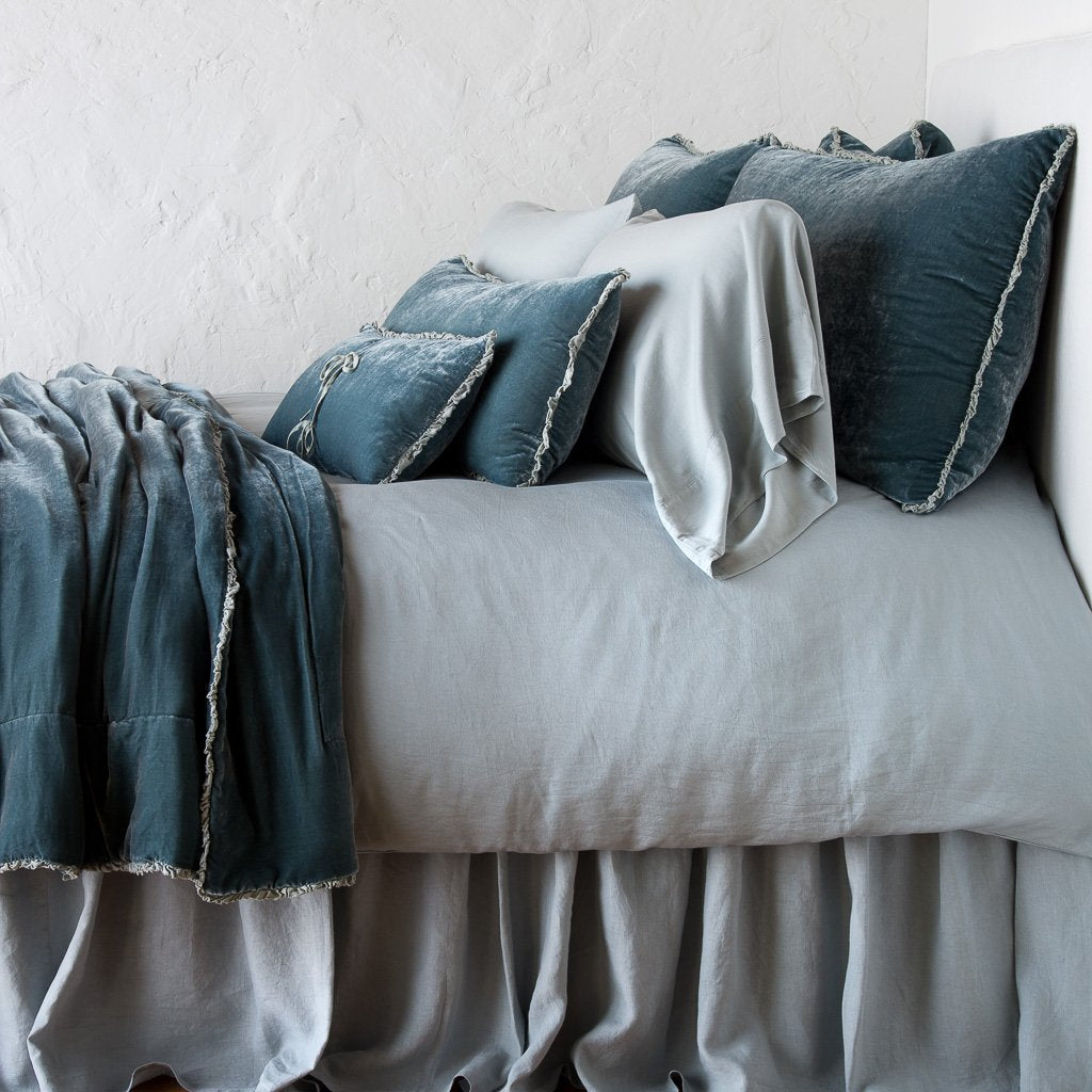 Mineral: Silk velvet throw blanket with petite ruffle, draped across a monochromatic bed - side view.