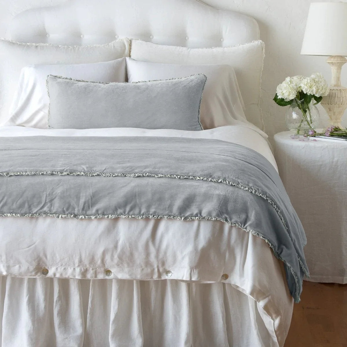 Sterling: Silk velvet shams with a petite ruffle on a white bed, stacked behind sleeping and throw pillows - view from end of bed.