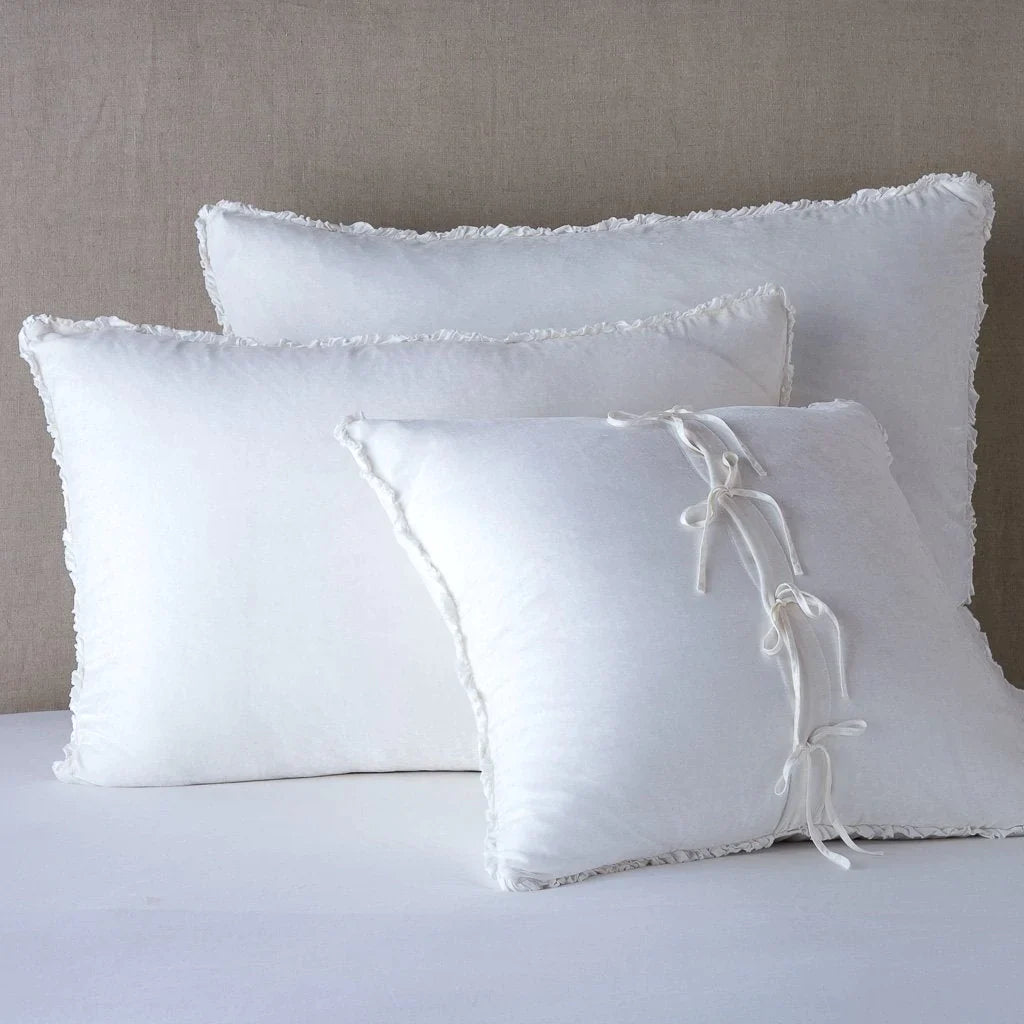 White: : Silk velvet shams with a petite ruffle leaning upright against a neutral headboard. The front sham is backwards, showcasing the charmeuse tie closures.