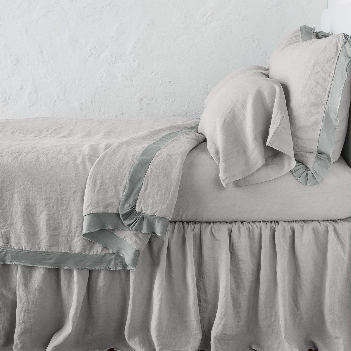 Fog: satin trimmed linen coverlet on monochromatic bed with corner pulled back to reveal sheet, bed skirt - side view.