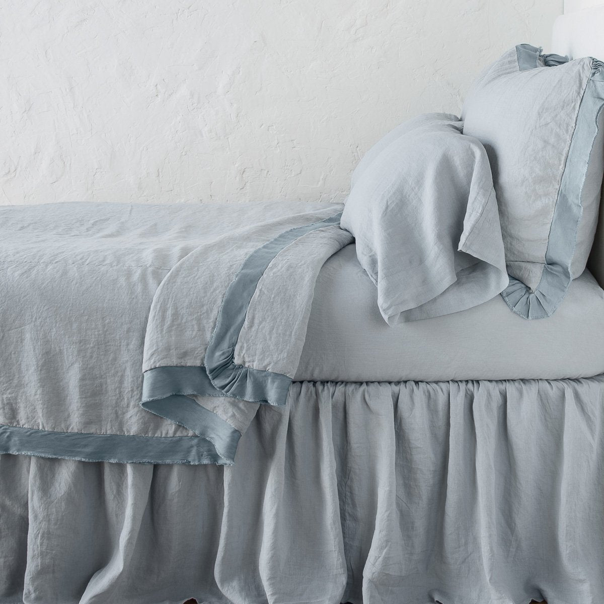 Mineral: satin trimmed linen coverlet on monochromatic bed with corner pulled back to reveal sheet, bed skirt - side view.