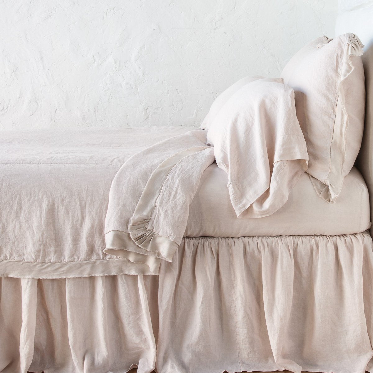 Pearl: satin trimmed linen coverlet on monochromatic bed with corner pulled back to reveal sheet, bed skirt - side view.