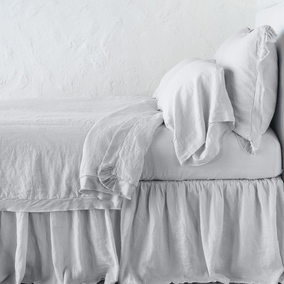 Sterling: satin trimmed linen coverlet on monochromatic bed with corner pulled back to reveal sheet, bed skirt - side view.