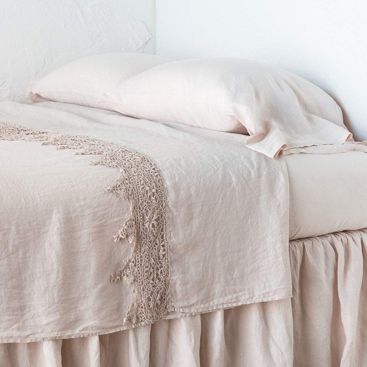 Pearl: Lace trimmed linen flat sheet neattly folded back on a monochromatic linen bed - cropped three-quarter angle.