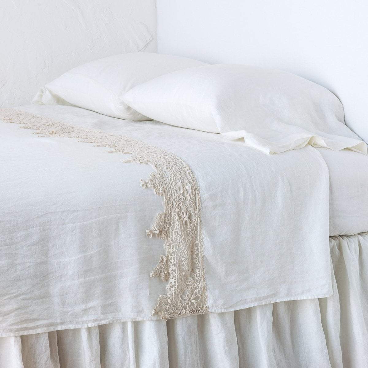 Winter White: Lace trimmed linen flat sheet neattly folded back on a monochromatic linen bed - cropped three-quarter angle..