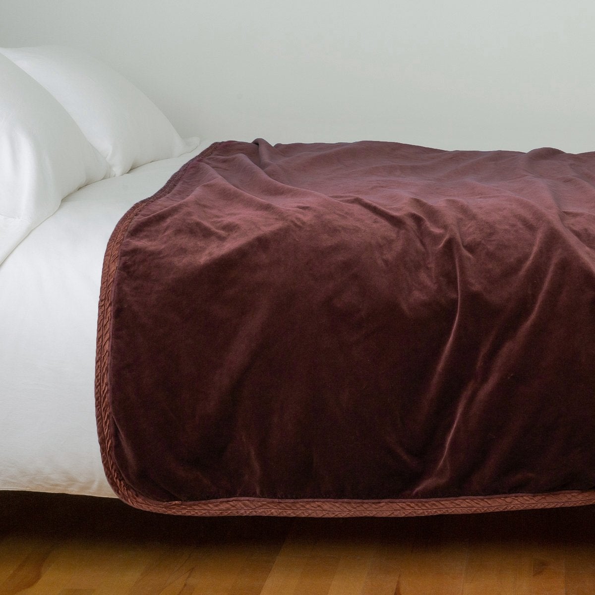 Mahogany: Cotton velvet bed end sized blanket, draped on a white bed - side view.