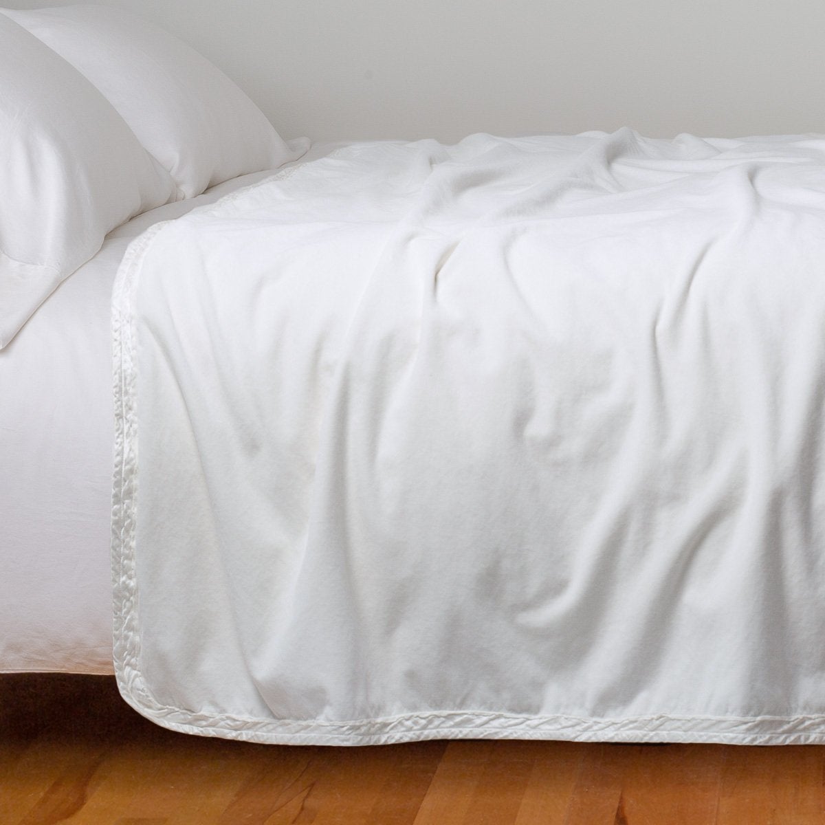 White: Cotton velvet bed end sized blanket, draped on a white bed - side view.
