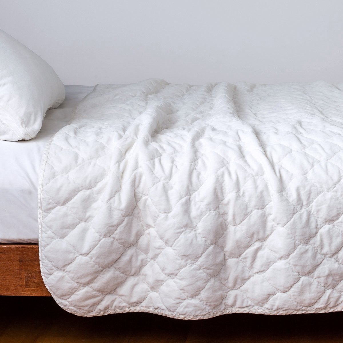 White: Quilted cotton velvet coverlet draped over a white fitted sheet - side view.