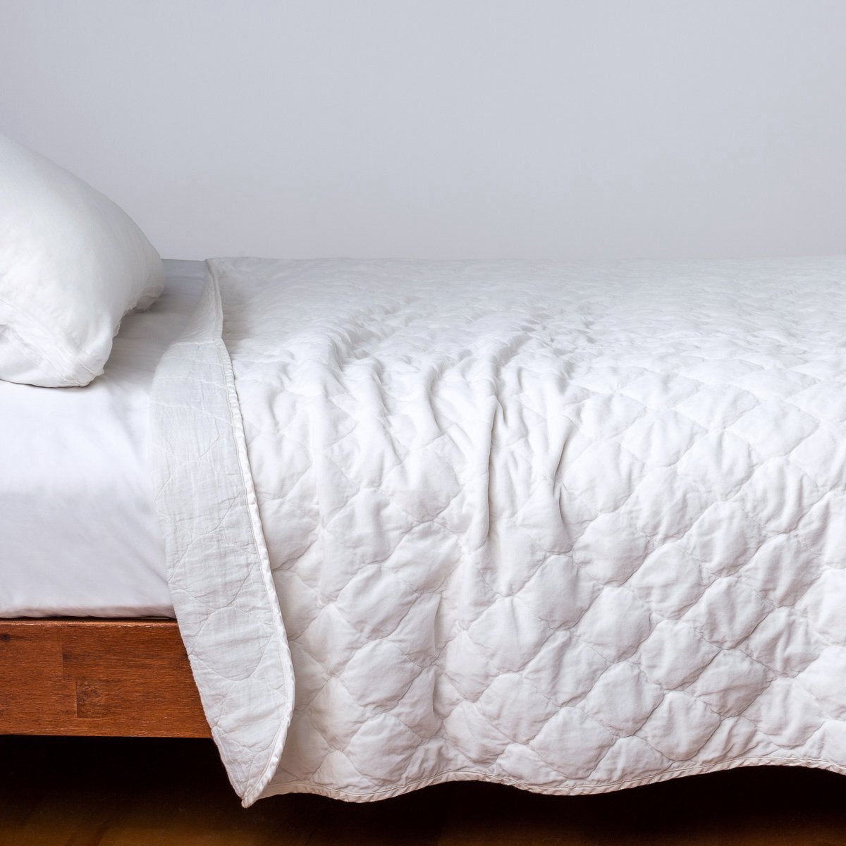 White: Quilted cotton velvet coverlet, with top folded back to showcase linen back, draped over a white fitted sheet - side view.