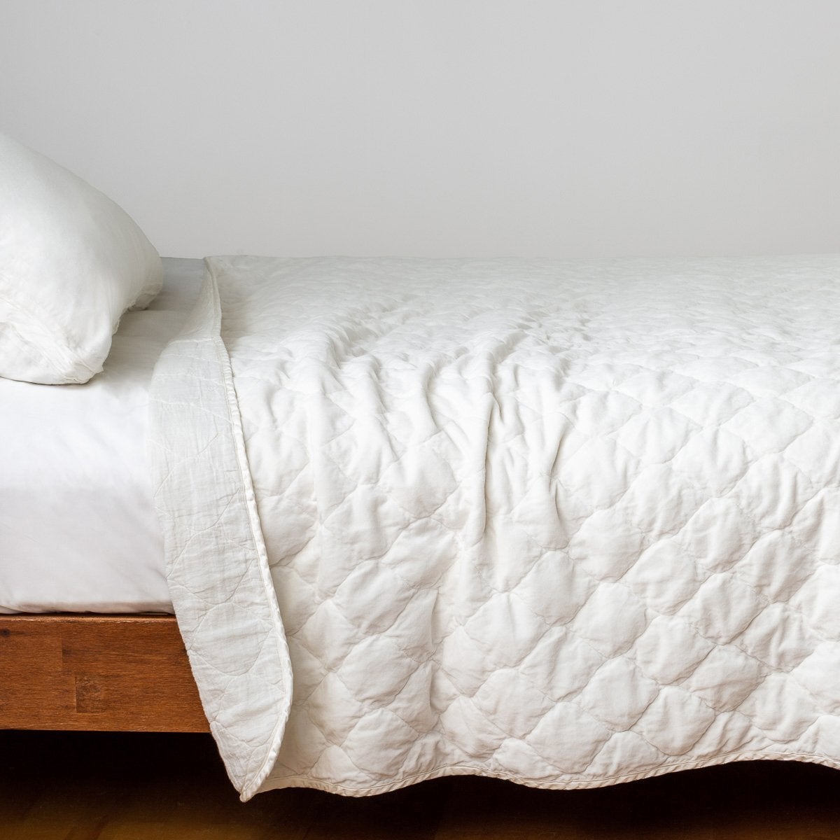 Winter White: Quilted cotton velvet coverlet, folded back to showcase linen back, draped over white sheeting - side view.