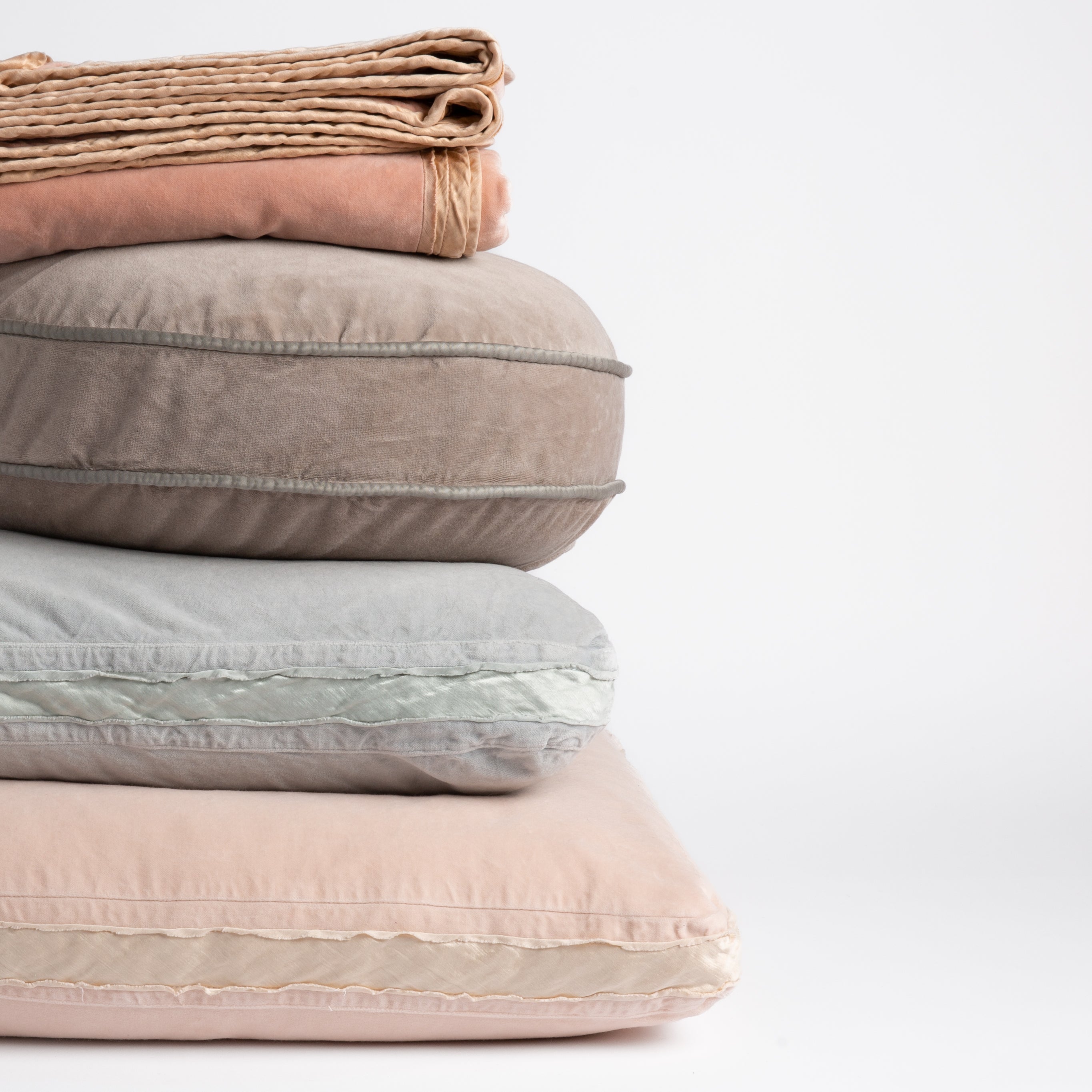 : stack of cotton velvet living pieces: throw blanket in rouge, 18" round pillow in fog, 18" square in cloud and 24" square pillow in pearl straight on against a white background. The different trim details visible on each piece.