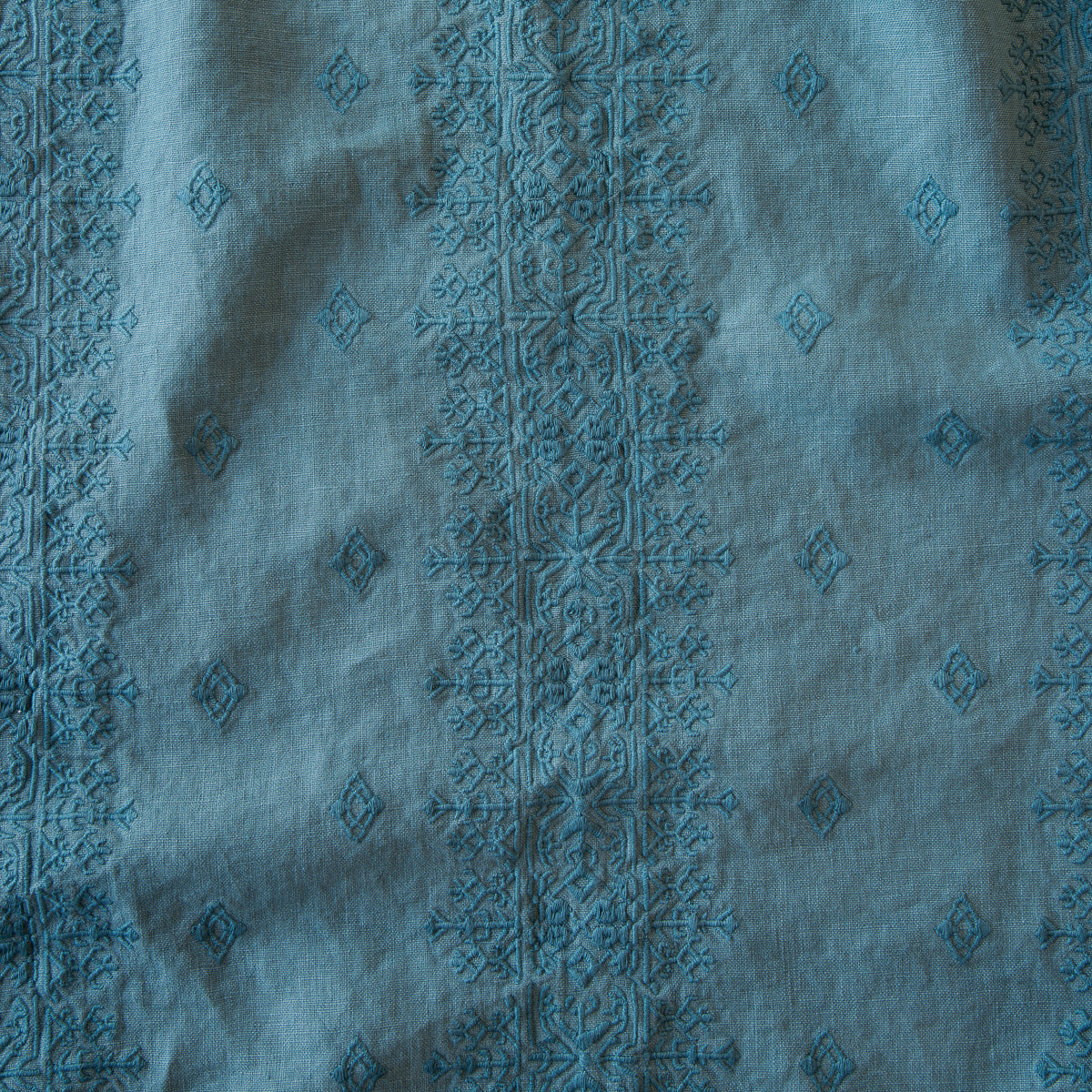 Cenote: A close up of Ines, midweight linen with cotton embroidery, in cenote, a vibrant, ocean-inspired blue-green.