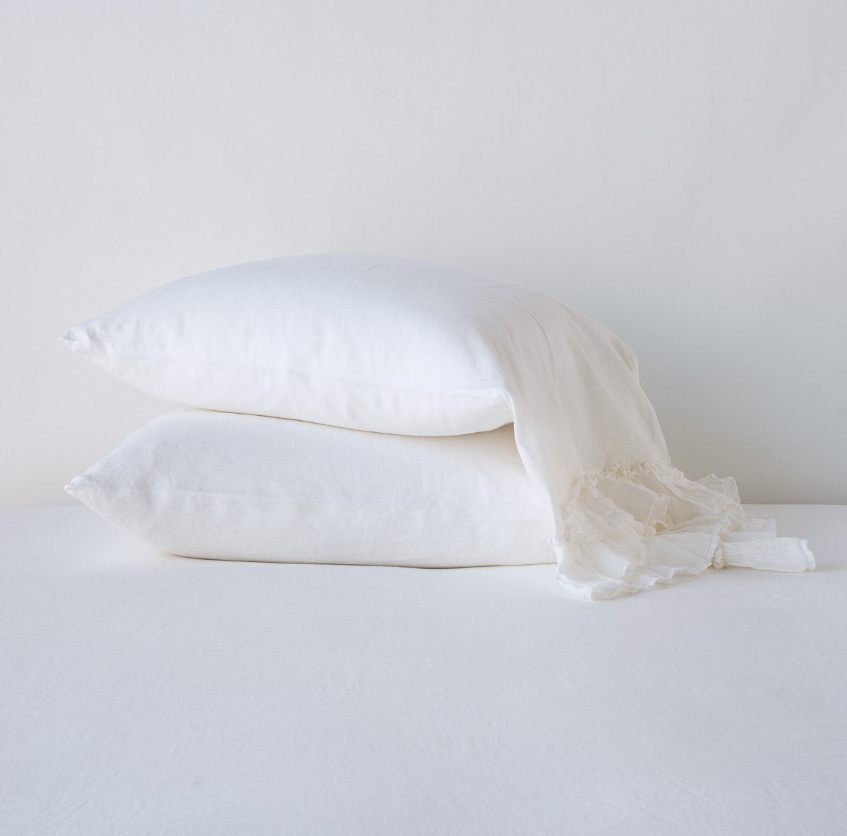 White: Two sleeping pillows stacked at a slight angle against a plain background, showcasing ruffle trim detail - side view.