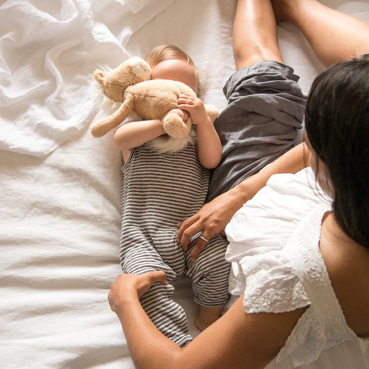 : Woman and baby lounging in bed with white linen sheeting - overhead view.