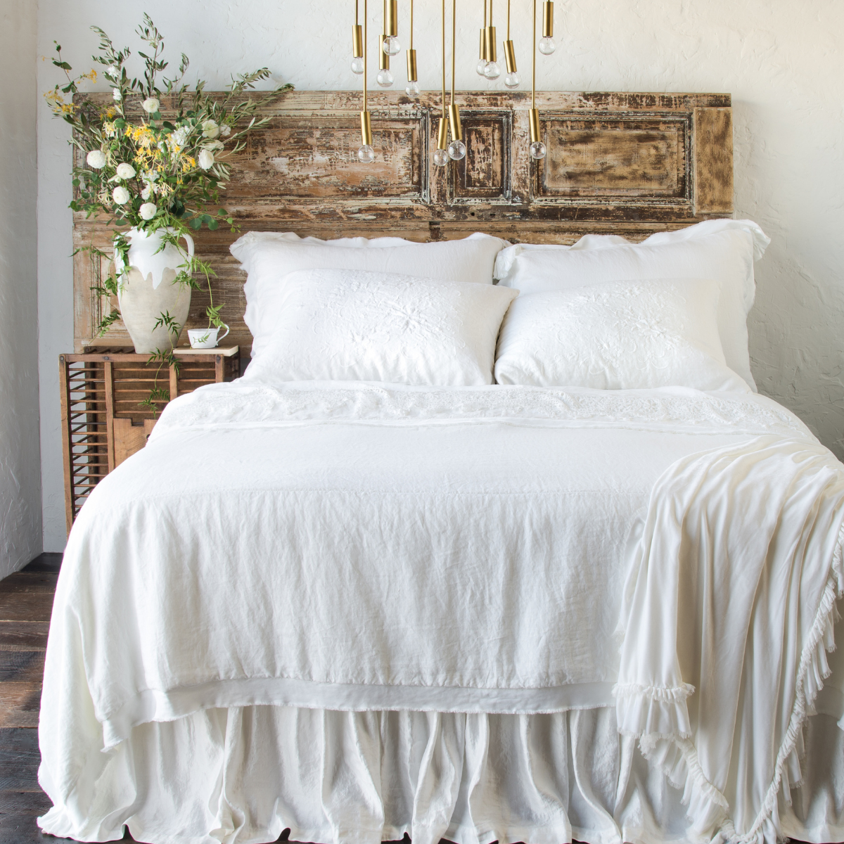 : Loulah throw blanket draped over the the corner of an all-white bed against distressed wooden headbaord - end of bed view.