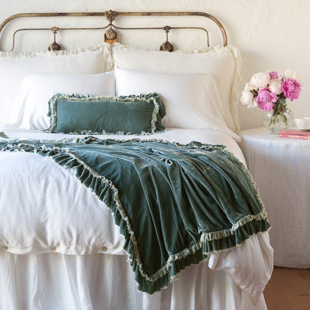 Eucalyptus: throw blanket draped over the end of a white bed, shown with matching accent pillow - end of bed view.