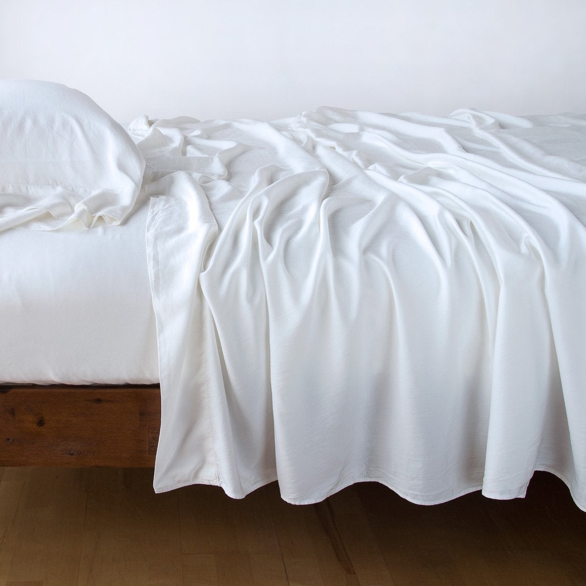 White: Rumpled flat sheet with matching fitted sheet and sleeping pillow - side view.