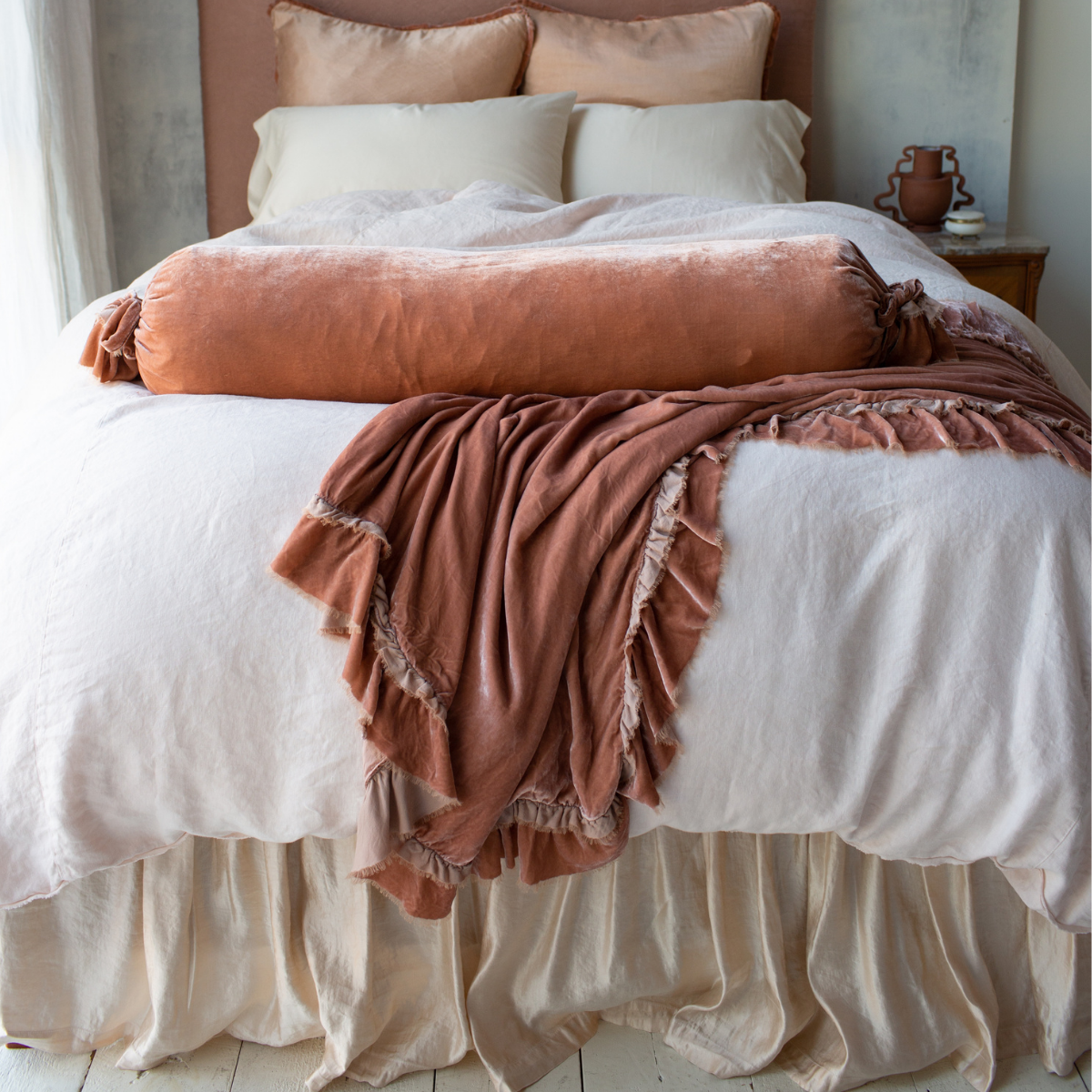 : Paloma bed skirt and matching shams add subtle shine to linen and cotton bedding accented with ruffled silk velvet, all in pink and cream tones - end of bed view.