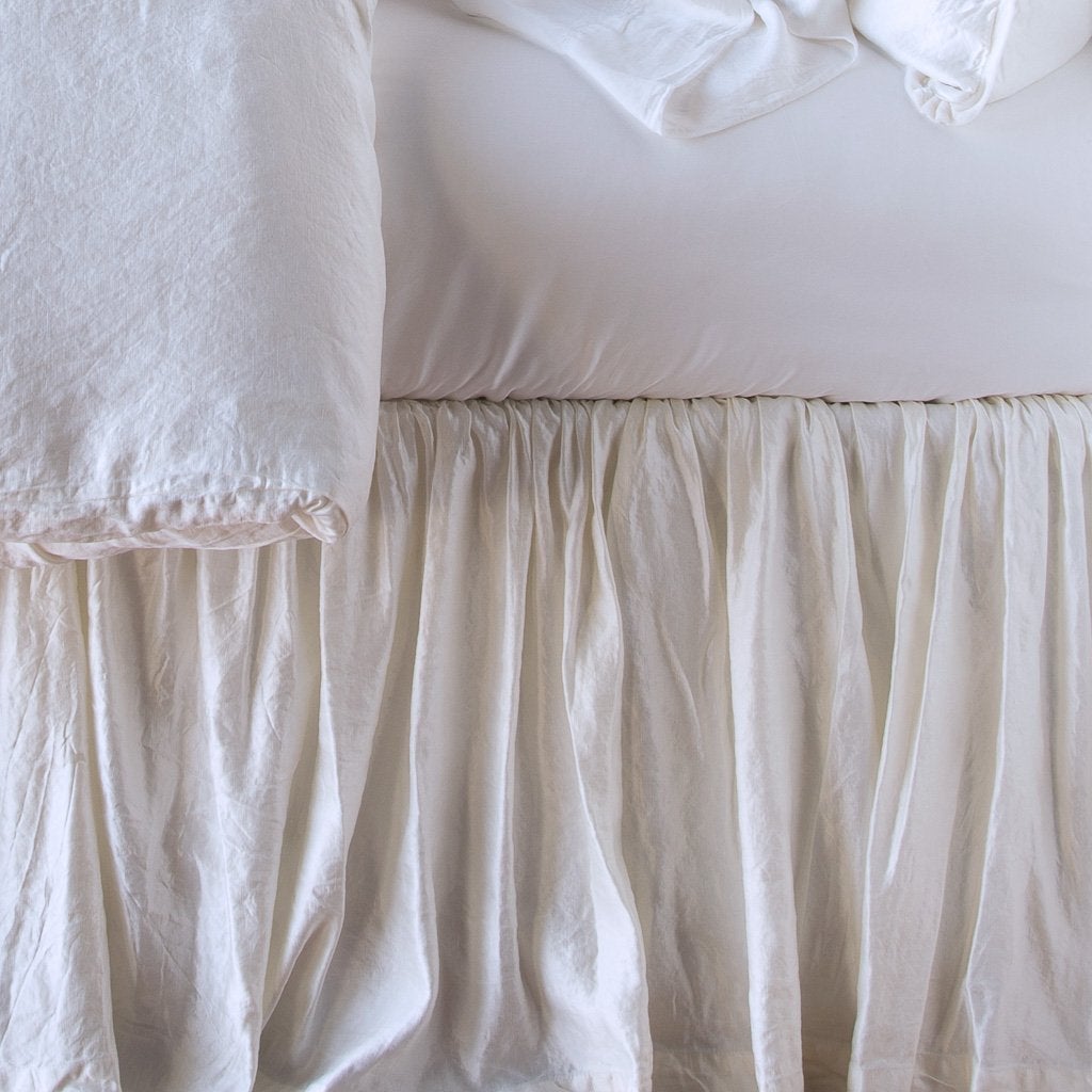 : Close up of Paloma bed skirt, highlighting the shimmering fabric and the gathering detail - white, side view.
