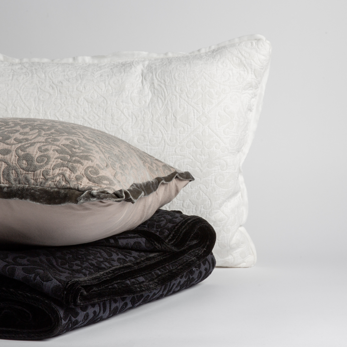 : throw pillows and blanket from the Vienna collection shown in white, fog and corvino against a white background.
