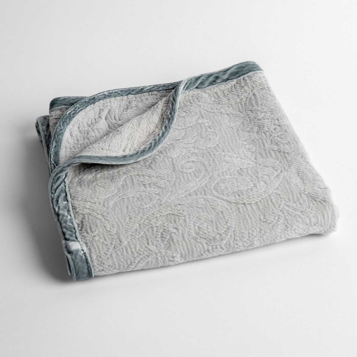 Cloud: a folded blanket with the corner turned down to show the trim against a white background, shot from an overhead angle. 