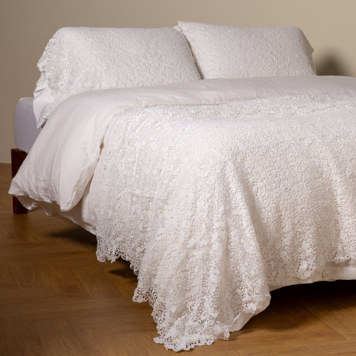 White: cotton lace bed scarf draped across the foot of a bed dressed in linen sheets and duvet cover in winter white -  shown with matching lace pillowcase covers over a linen liner in winter white. 