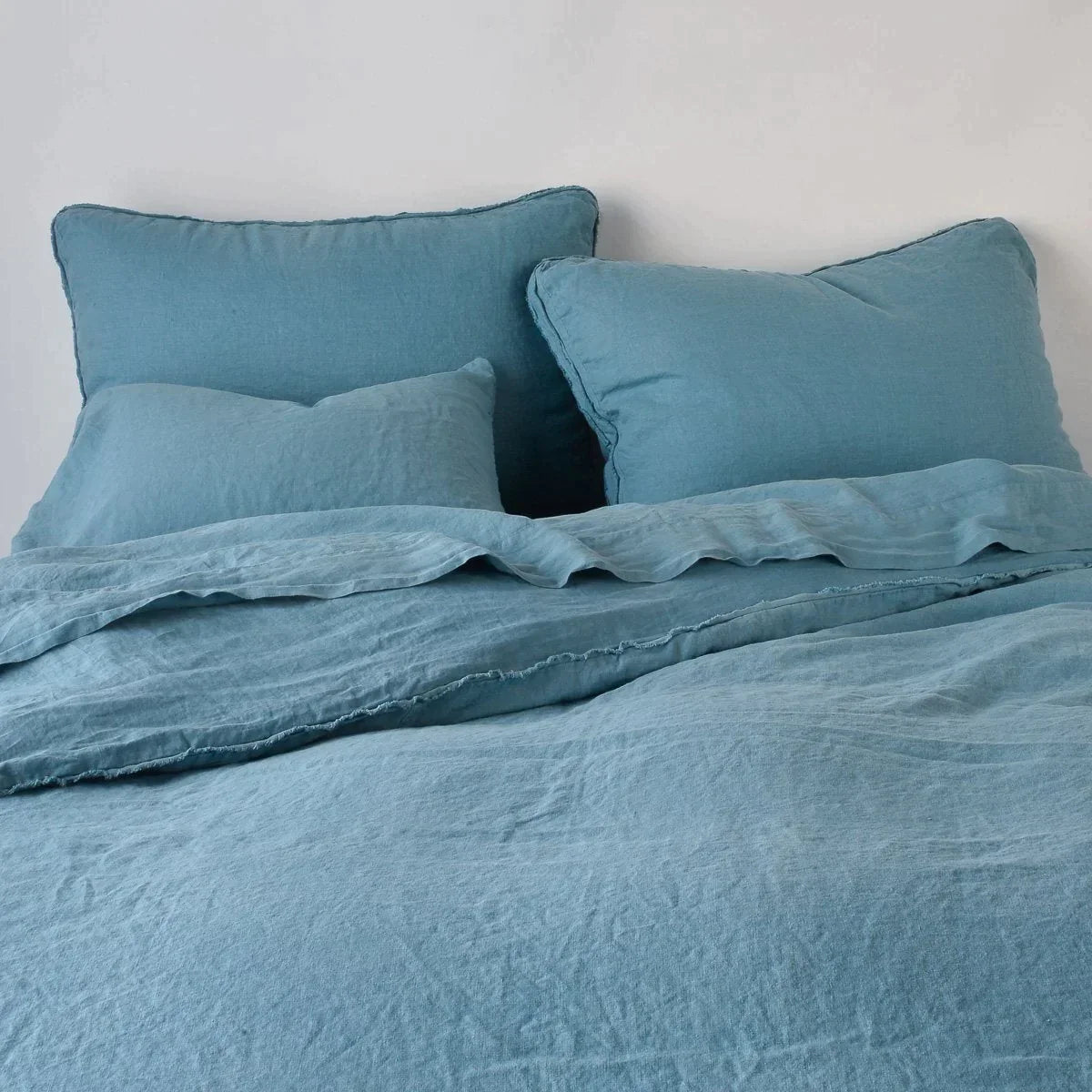 Cenote: Midweight linen shams shown from foot of bed, leaning against a plain background with monochromatic bedding. 