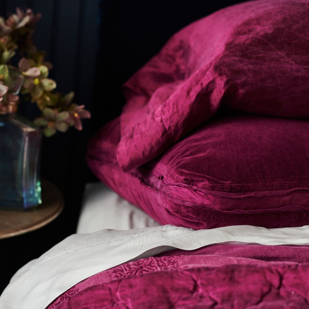 : Close-up of Paloma sleeping pillow stacked on a cotton velvet sham, on white sheets against a moody dark background.