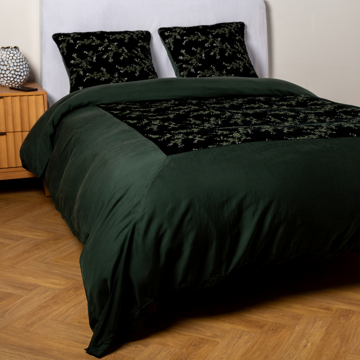 Juniper: A ¾ angle shot of an embroidered silk velvet and tencel duvet cover and matching shams with a vase and cell phone on the side table. 